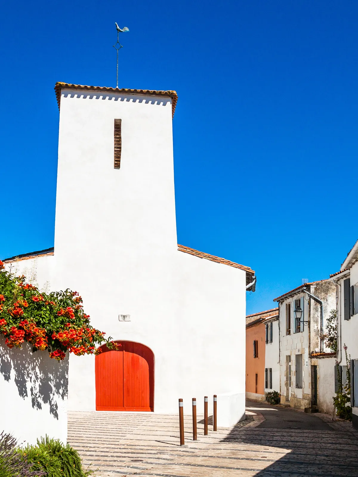 L’église des Portes-en-Ré, façade blanche et porte rouge, ruelle fleurie